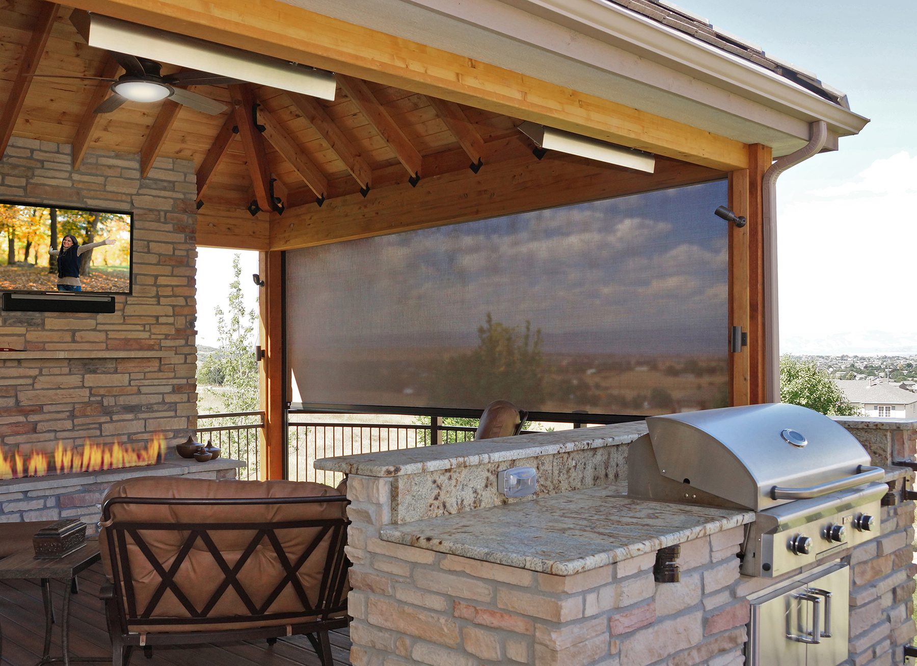 Exterior roller shade beside an outdoor fireplace and grill on a covered patio, outdoor living for Frisco and Prosper homes