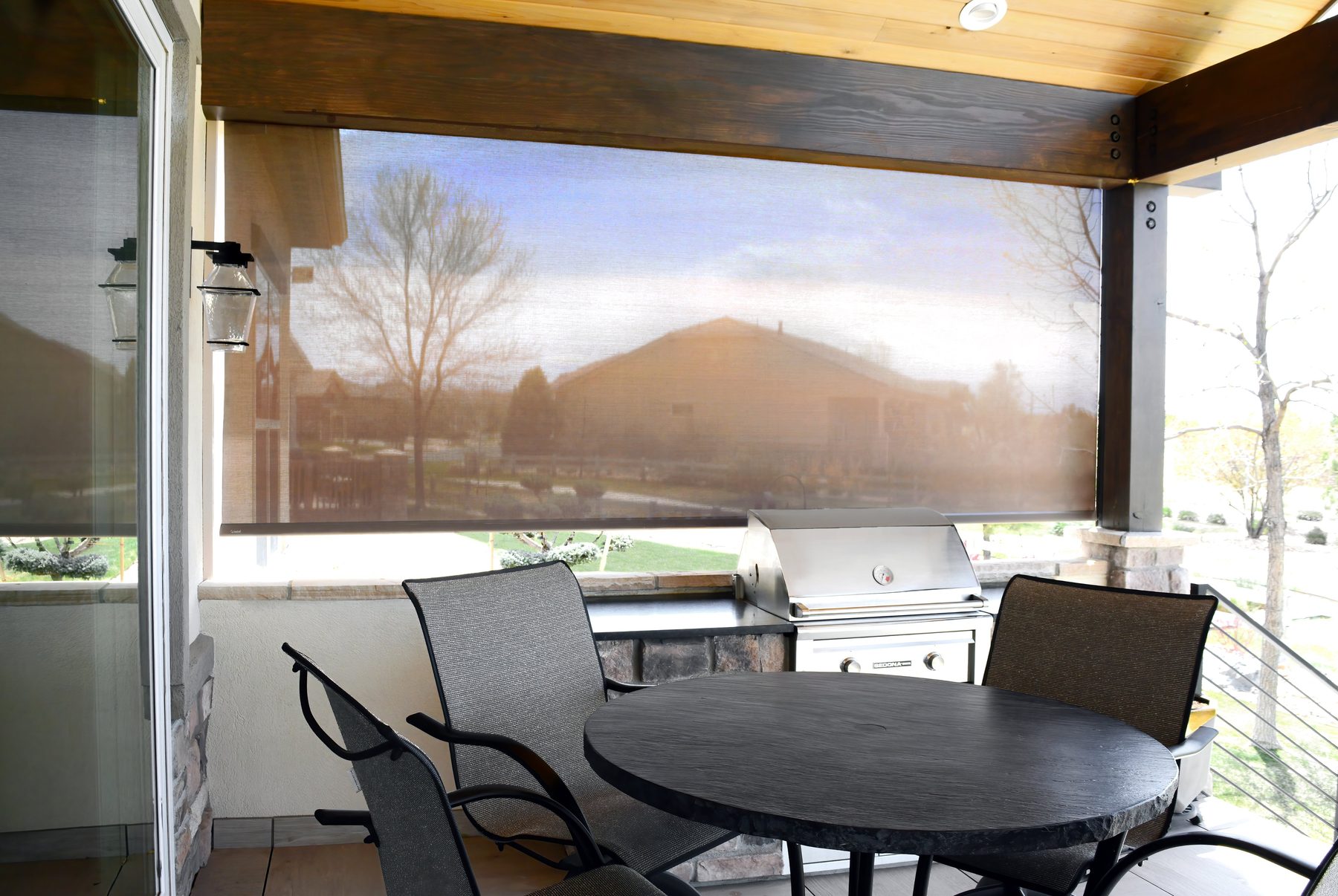 Solar roller shade over a grill and bistro table on a covered patio in a North Texas neighborhood